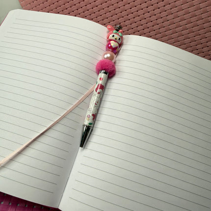 Pink pastel bunny beaded pen with black ink resting on an open lined journal, styled for cozy girly desk décor.