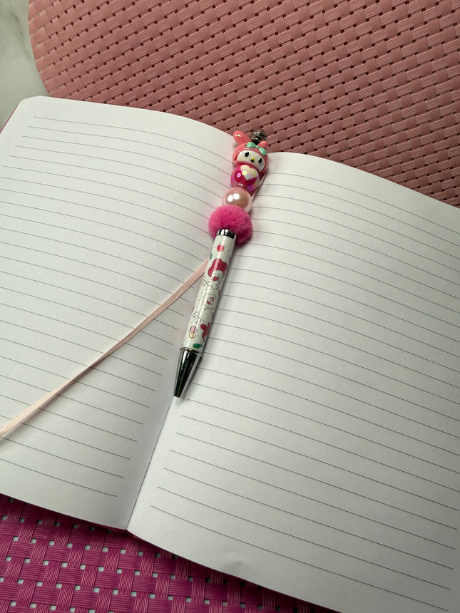 Pink pastel bunny beaded pen with black ink resting on an open lined journal, styled for cozy girly desk décor.