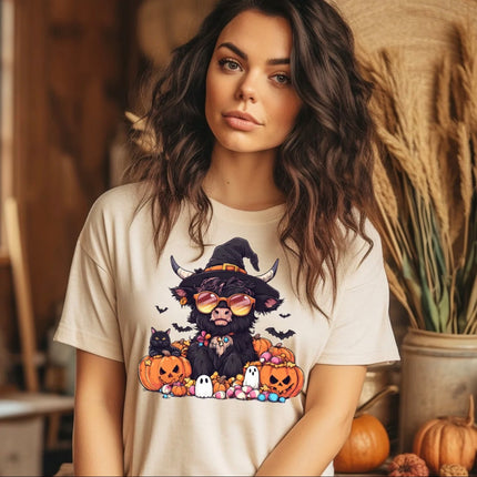 Cream Halloween T-shirt with black Highland cow wearing witch hat and sunglasses surrounded by pumpkins, candy, ghosts, bats and black cat.