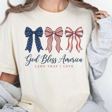 Person wearing a cream sweatshirt with 'God Bless America Land That I Love' text and three bow designs.