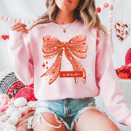 Person wearing a pink sweatshirt with a large bow design, sitting in a decorative setting.